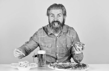 Neşeli sakallı hippi adam pizza yiyor. Pizza partisi konsepti. Mutluluğu ağıza vermek. Bira ve yemek. Barda akşam yemeği. Aç adam pizza yiyecek ve bira içecek. Pizzacı