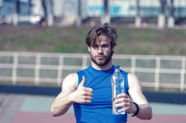 Yakışıklı kaslı adam elinde su şişesiyle baş parmağını kaldırıyor.