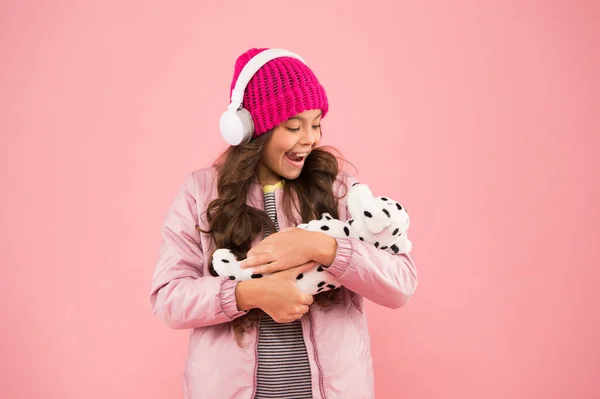 Amo a mi cachorro. ropa de abrigo para el clima frío. niña feliz jugar juguete de perro. rosa es su color favorito. niño pequeño escuchar auriculares de música. pelo rizado largo del niño. temporada de invierno acogedor. cuidado de mascotas — Foto de Stock