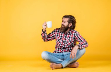 Beyaz bardak tutan yakışıklı sakallı adam. Bardakla içecek. Çay ya da kahve içmek. Günaydın. Evde sabah havası var. İlham konsepti. hippi adam kahve içer.