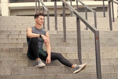 Kendine güvenen bir sporcunun portresi. Genç sporcu iyi bir koşudan sonra dışarıda oturuyor. Spor giyim bölümünde genç bir adam. Eğitimden sonra rahatla. Adam merdivenlerde oturuyor. Düşünceli, güçlü adam oturuyor.