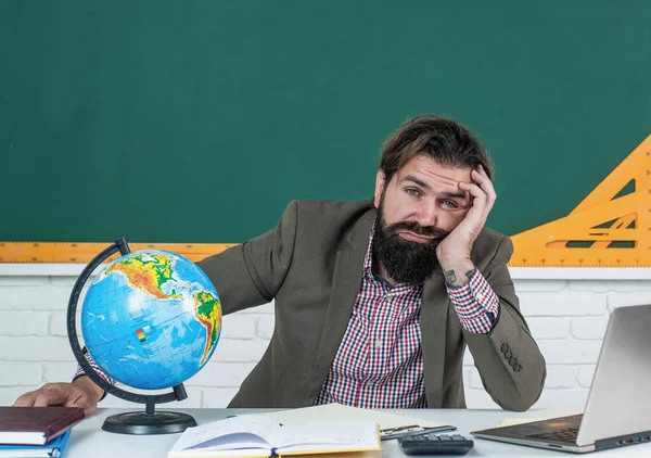 mature bearded man teacher in costume sit in school classroom with geography globe map, education