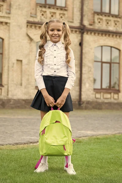 Boldog óvodás lány hátizsákkal az iskola udvarán. Vissza az iskolába. A gyerek egyenruhában viszi az iskolatáskát. az oktatás fogalma. gyermekkor fejlődése. Boldog lány aranyos mosoly — Stock Fotó