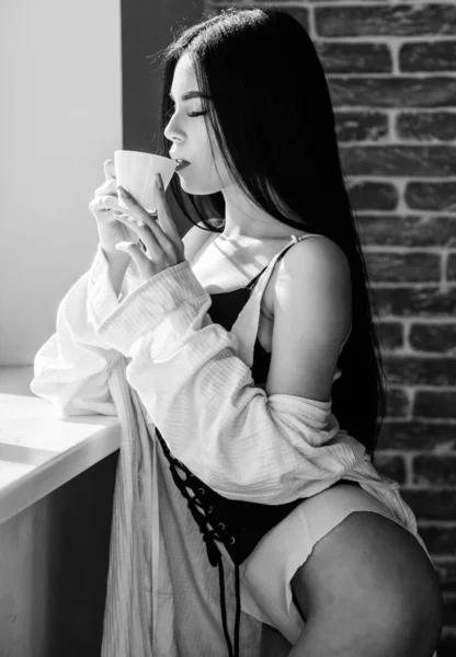 Seksi göğüslü seksi kız pencere kenarında kahve içiyor. Çekici kadın iç çamaşırları evde dinleniyor. Tutkulu gizemli aşık. Kahve zamanı. Ama önce kahve. Sabah güneşinin tadını çıkarıyorum. — Stok fotoğraf