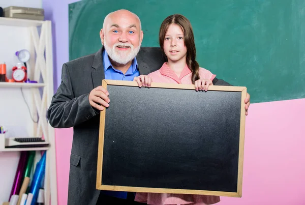 Because Experience Matters. mature teacher and happy pupil girl. empty chalk board. School sales. school classroom. small girl with man tutor study. blackboard for information and add. Copy space — Stock Photo, Image