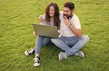 Neşeli çift dizüstü bilgisayar kullanıyor yeşil çimenler, yaz tatili konsepti