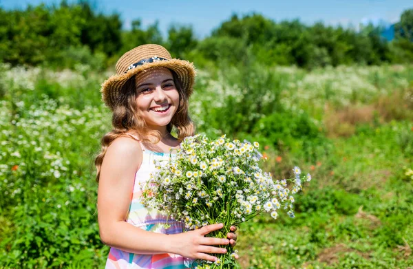 Glad liten flicka i sol hatt leende med kamomill blomma gäng på soligt sommarlandskap, semester — Stockfoto