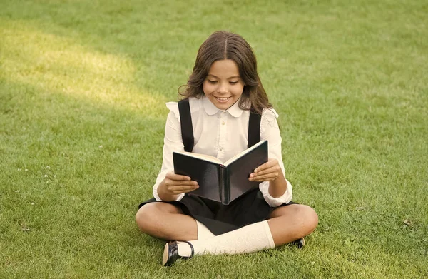 Šťastná školačka s knihou na školním dvoře. Zpátky do školy. Tvrdě pracující dítě s knihou. koncepce vzdělávání a čtení. rozvoj představivosti. roztomilá dívka číst knihu — Stock fotografie