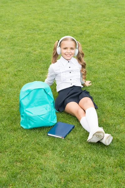 Menina adolescente feliz em uniforme ouvir fones de ouvido relaxando na grama verde depois da escola, música — Fotografia de Stock