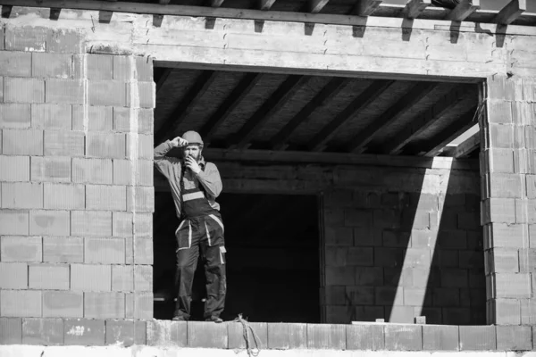 수리공은 현장에서 헬멧을 쓴다. 피곤 한건축가는 휴식을 취한다. 건설 노동자 흡연. 건축중에 있다. 군복을 입고 딱딱 한 모자를 쓴 남자. 평일 근무일 — 스톡 사진