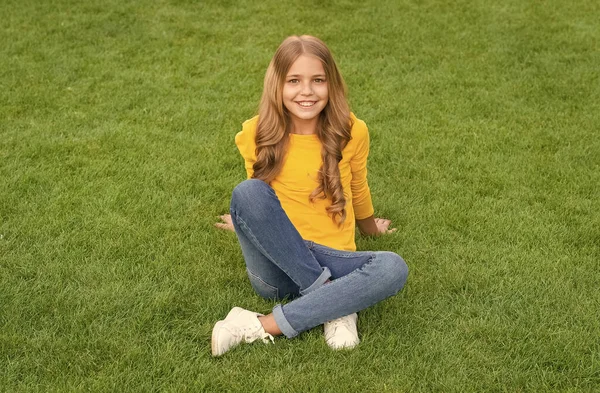 Gelukkig meisje heeft lang krullend haar. schoonheid en mode van kinderen. tienermeisje na kapper. ontspannen op groen gras. vrije tijd in de lente. Gelukkige jeugd. Jongen met stijlvol haar. vrolijke glimlach — Stockfoto