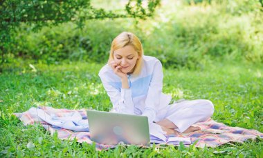 Dizüstü bilgisayarı ya da defteri olan bir kadın yeşil çimlerin üzerinde oturuyor. İş kadını serbest çalışan biri dışarıda çalışıyor. Çevrimiçi iş fikirleri kavramı. İş pikniği kavramı. Serbest çalışmaya başlamak için adımlar