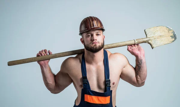 Hombre guapo usar ropa de trabajo y casco mientras se trabaja con la pala, obrero —  Fotos de Stock