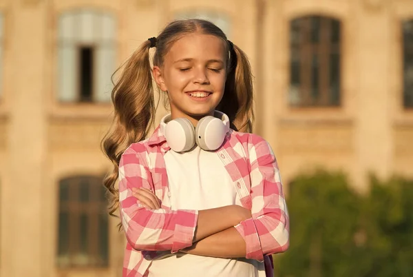 陽気な音楽愛好家。小さな女の子はチェッカーシャツを着て。日没時にヘッドセットを持った子供。子供の春と夏のファッション。幸せな子供時代。電子書籍でeラーニング。現代の技術 — ストック写真