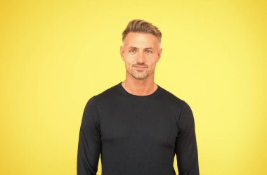 Onun yakışıklı olduğunu biliyor. Olgun bir adamın yakışıklı görünüşü. Yakışıklı adam sarı arka plan. Sıradan bir tarz. Moda trendleri. Erkekler tımar ediliyor. Cilt rutini. Berber dükkanı. Tıraşsız ama yakışıklı.