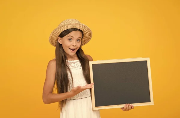 Precisas deste produto para a escola. Menina feliz apresentando produto. Criança segura o quadro-negro da escola. Produto para venda. Promoção de produtos. Blackboard vazio para texto publicitário, espaço de cópia — Fotografia de Stock