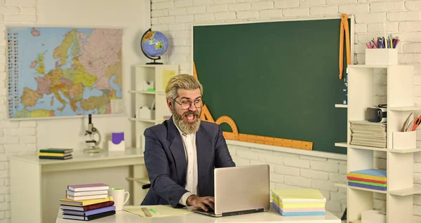 Dzień wiedzy. Nauczyciel w szkole siedzi w klasie. Przystojny hipsterski dojrzały inteligentny pedagog. Użyj laptopa i internetu. Oficjalnie złożony wniosek online. Praca domowa. Wracamy do szkoły. — Zdjęcie stockowe