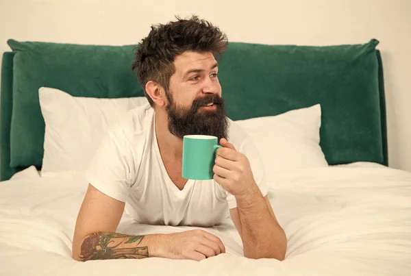 De buen humor. El hombre barbudo bebe café matutino en la cama. Hipster disfrutar de la bebida caliente en la mañana. Té de desayuno. A primera hora de la mañana —  Fotos de Stock