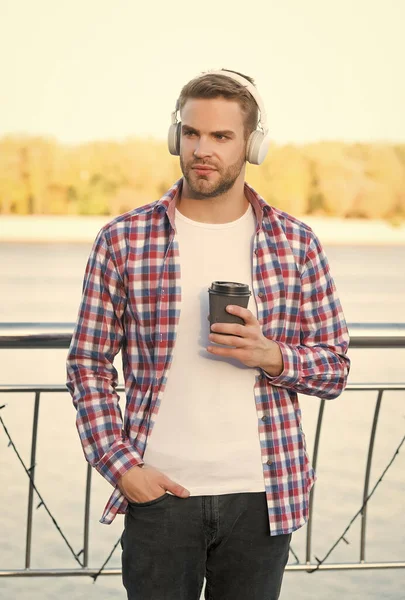 Young man student in casual shirt and headset listen ebook and music drink fresh aromatic coffee while walking outdoor, daily routine — Stock Photo, Image