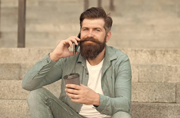 A trazer energia para as vossas manhãs. Um homem barbudo bebe café ao telefone. O café leva-nos. Pausa para café ao ar livre. Café e comunicação. Nova tecnologia. Vida moderna — Fotografia de Stock