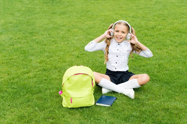 Šťastné dospívající dívka poslouchat hudbu sedí na zelené trávě po škole, sluchátka — Stock fotografie