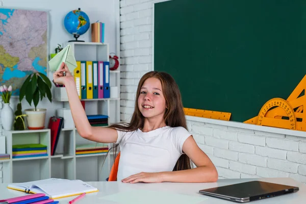 Lachende tiener meisje spelen met papier vliegtuig in schoolklas, jeugd — Stockfoto