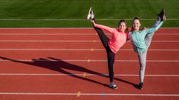 Ginastas adolescentes felizes fazem divisões verticais segurando pernas na pista de atletismo, espaço de cópia, ginástica — Fotografia de Stock