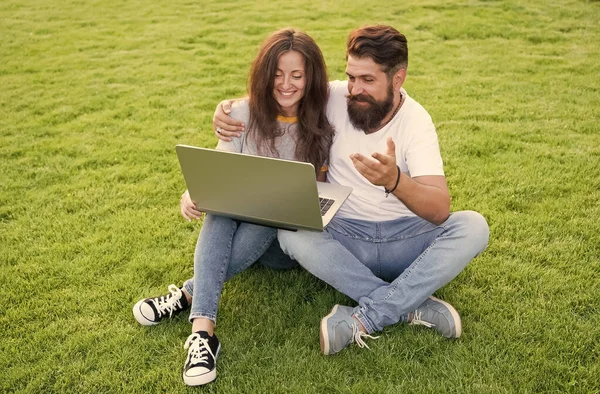 Modern eğlence. Sakallı adam ve seksi kadın dizüstü bilgisayar kullanıyor. Birbirine aşık bir çift yeşil çimlerin üzerinde dinleniyor. Modern bilgisayar teknolojisinin tadını çıkarıyorum. Modern hayat. Sosyal medya. Modern bir eğlence. Yaz tatili — Stok fotoğraf