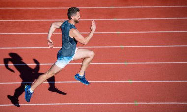 Enerjik atletik kaslı adam koşucu açık hava stadyumunda yarış pistinde koşuyor, acele et.