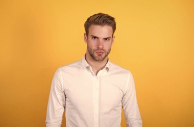 Saf güven. Turuncu arka planda genç, seksi maço. Resmi giyinmiş kendine güvenen bir iş adamı. Ofis tarzı. Erkek güzellik standardı. Sıradan bir iş adamı. Yakışıklı, tıraşsız adam beyaz gömlek giyiyor.