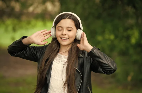 Má uši pro hudbu. Šťastné dítě nosí sluchátka venku. Malá holka poslouchá hudbu ve sluchátkách. Pohodlné ušní chrániče. Chrániče uší. Slyším ochranu. Nová technologie. Moderní život — Stock fotografie