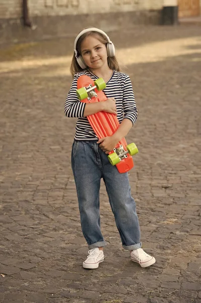 Petit enfant tenir penny skateboard écouter de la musique dans les écouteurs modernes été urbain en plein air, le sport — Photo