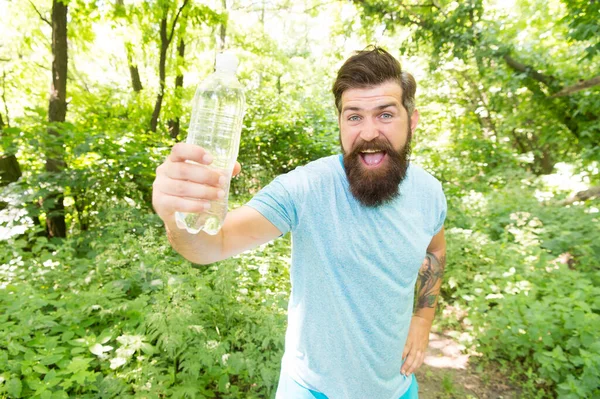 Glad skäggig man i sommarkläder visar vattenflaska i skogen, selektivt fokus, vattenbalans. — Stockfoto