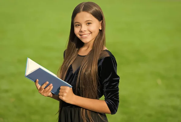 Feliz niño pequeño en uniforme escolar sonrisa celebración estudio libro verde hierba soleado verano al aire libre, educación —  Fotos de Stock