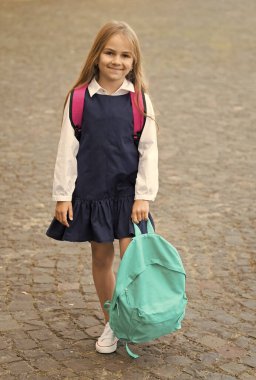 Moda üniformalı küçük mutlu çocuk dışarıda sırt çantası tutuyor, okula geri dönüyor.