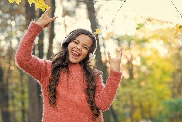 Impazzire. bambino ascoltare musica nella foresta autunnale. godere di elearning in cuffia. bambino indossare maglione nel parco autunnale. bambino felice rilassarsi nella natura autunnale. piccola ragazza indossare le cuffie. educazione scolastica moderna — Foto Stock