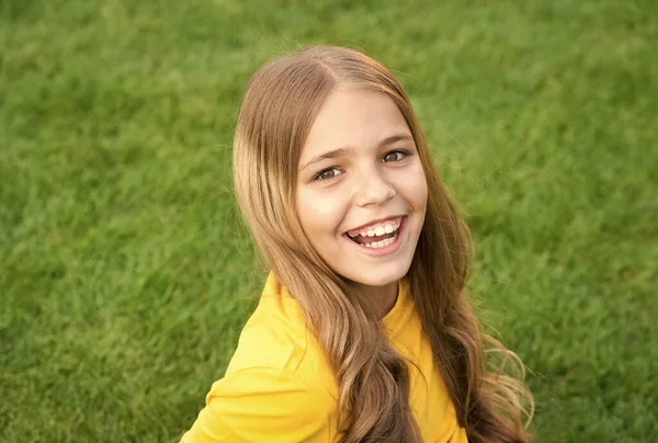 Cuidados faciais. criança beleza e moda. menina adolescente após cabeleireiro. relaxar na grama verde. tempo de lazer primavera. infância feliz. criança com cabelo elegante. Sorriso alegre. menina feliz tem cabelo encaracolado — Fotografia de Stock