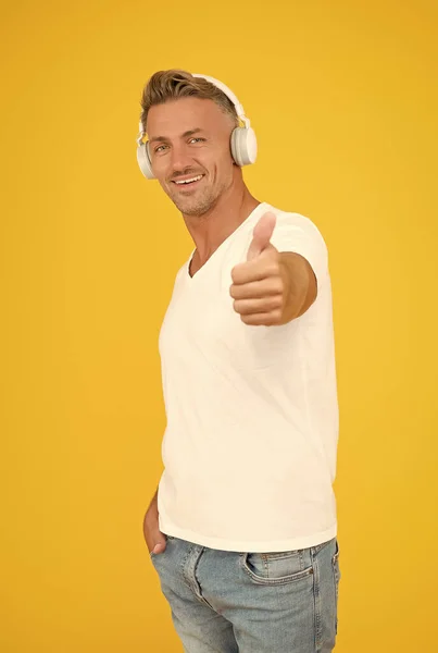 Weil Ihre Ohren das Beste verdienen. Schöner Mann gibt Daumen nach oben gelben Hintergrund. Kopfhörertechnologie. Zustimmungszeichen. Musik hören. Moderner Lebensstil. Genehmigungsverkauf — Stockfoto