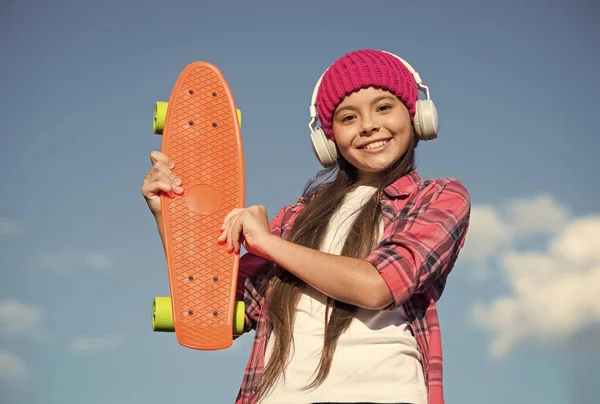 幸せな女の子子供ホールドペニーボードリッスン音楽でヘッドフォン晴れ空屋外,輸送 — ストック写真