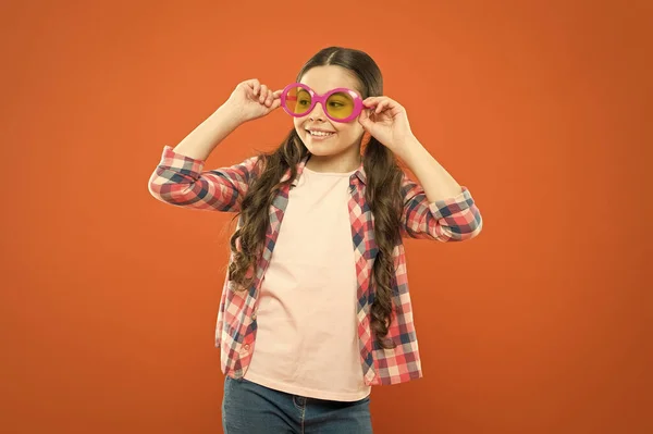 Модні сонцезахисні окуляри підтримують захист очей дітей і добре виглядають. Невелика модель моди на помаранчевому фоні. Чарівна маленька дівчинка в модному аксесуарі. Мила дитина з модним виглядом — стокове фото