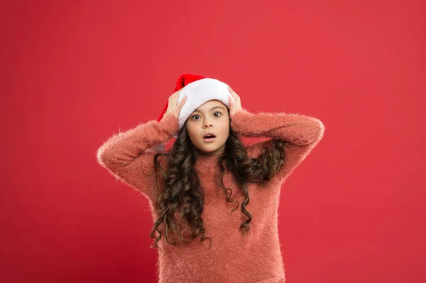 oh my god. little santa. happy new year. time for christmas holiday. small girl in santa hat. surprised child red background. winter kid fashion. favorite winter holiday. having fun