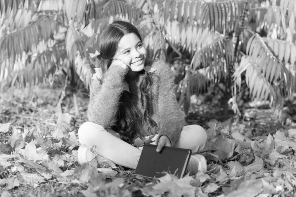 Iskolát hoz a természetbe. Aranyos általános iskolás gyerek könyv ül sárga levelek. Boldog kislány vissza az iskolába ősszel. Suli után. Szeptember 1. — Stock Fotó