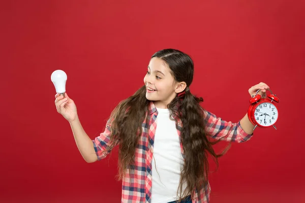 Inspirado criança segurar relógio fundo vermelho. Inspiração e brainstorming. Energia eléctrica. Menina segurar lâmpada. Bonito criança busca inspiração. Tempo de iluminação. Ideia e inspiração — Fotografia de Stock