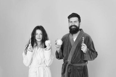 Sağlıklı ve güçlü dişlere sahip olmak. Sabah rutini. Sabah kişisel bakım. Bornoz giymiş çiftler. Sakallı adam ve kız sağlıklı bir gülümseme. Aile çifti diş fırçasıyla elma tutuyor.