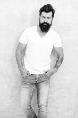 Hırslı adam. Sakallı adam erkeklik saçıyor. Fiziksel çekicilik. Yakışıklı hippi pantolonu. Erkek moda trendleri. Basit ve sıradan bir yaz. Acımasız maço gri arka plan. Erkek şiddeti.