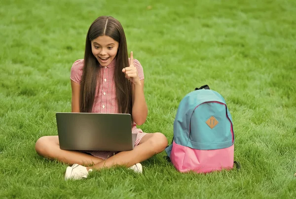 Inspirerade glada barn med hjälp av dator för online-skola studie sitter i parken på grönt gräs med ryggsäck, utbildning — Stockfoto