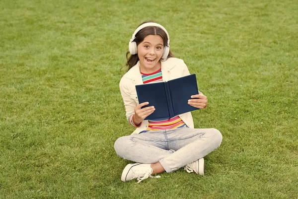 Pracuj tvrdě. Malá holčička čte knihu. literatura pro děti. psát vzpomínky z dětství. chytrý kluk ve sluchátkách. Zpátky do školy. děti studují online v parku. poslouchat hudbu na zelené trávě s knihou — Stock fotografie