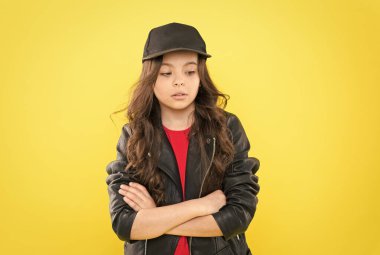 Uzun boylu, esmer, kendine güvenen küçük bir kız çocuğu gündelik moda tarzında giyiniyor. Kollarını çapraz sarı arka plan, kendine güven.