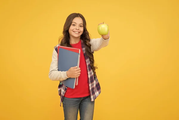 Τα σνακ με φρούτα θα αλλάξουν την εμφάνισή σου. Ευτυχισμένο παιδί κρατά μήλο και βιβλία κίτρινο φόντο. Σχολικές διακοπές. Ο καρπός της γνώσης. Διατροφή και αγωγή υγείας. Υγιεινή τροφή. Γίνε θρεπτικός — Φωτογραφία Αρχείου