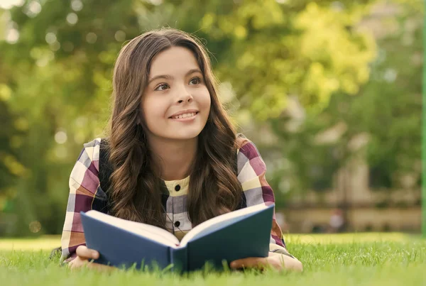 Čtení pomáhá růst vašeho semene znalostí. Šťastné dítě čte knihu ležící na zelené trávě. Den znalostí. 1. září. Zpátky do školy. Základní vzdělání. Školní knihovna. V mimoškolním klubu. Rozšiř svou mysl — Stock fotografie